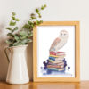 Sur un bureau un cadre avec une aquarelle d'une chouette effraie posée sur des livres